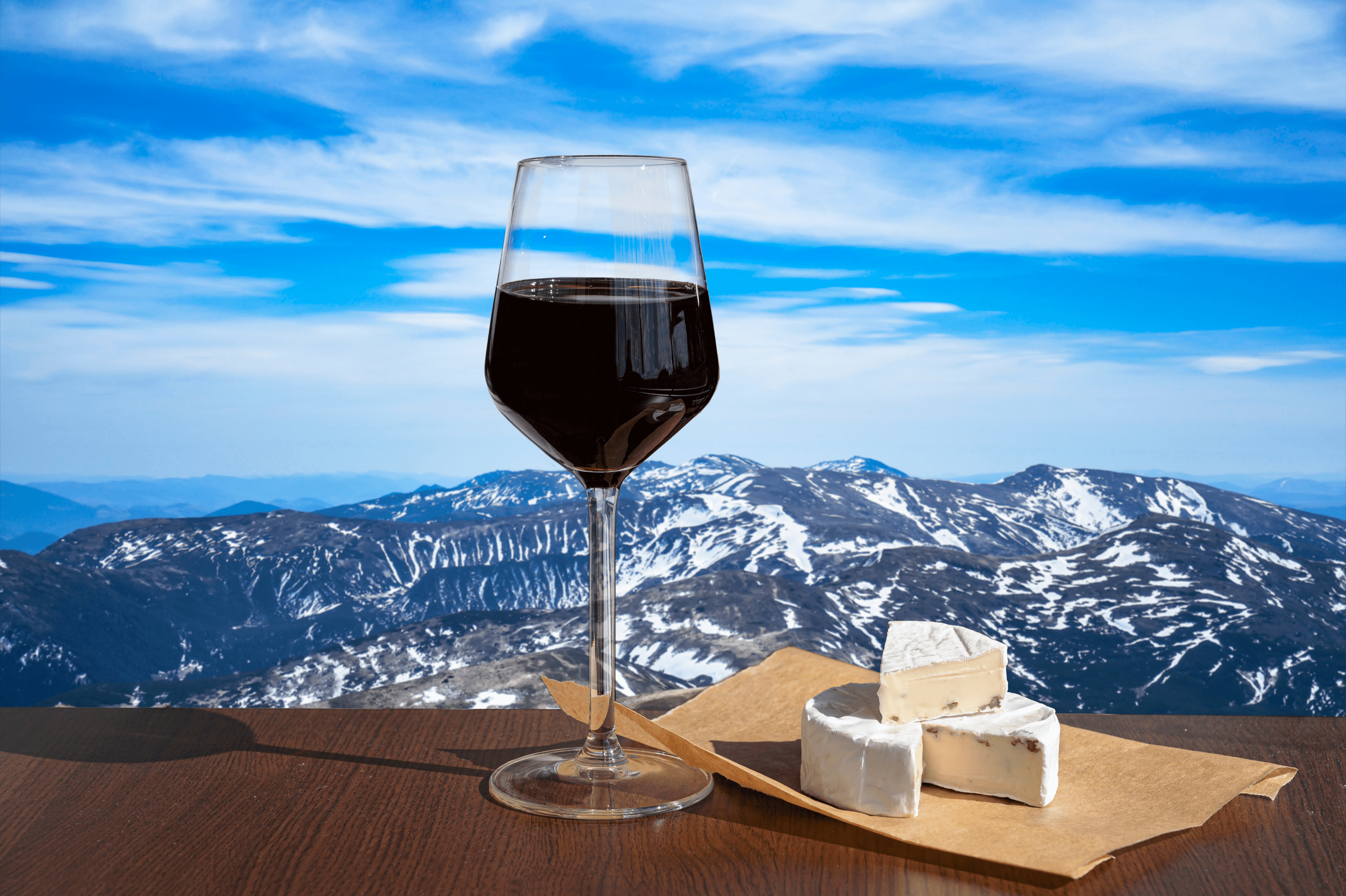 Verre de vin rouge et plateau de fromage devant une vue de montagnes enneigées